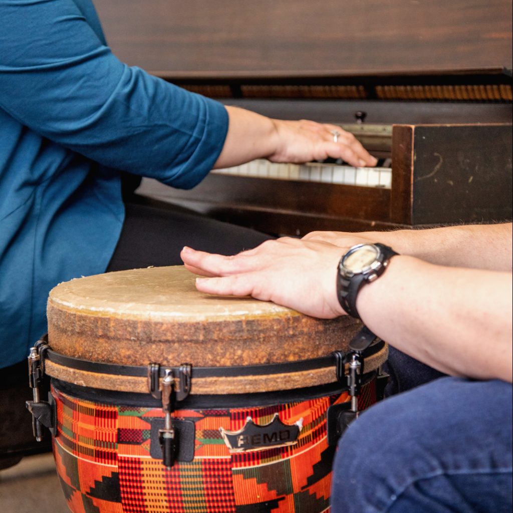 A certified music therapist is improvising with a client who is playing a djembe drum.